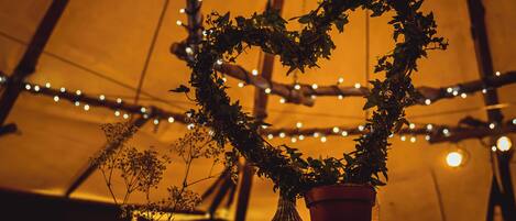 A heart-shaped arrangement of greenery in a vase, with string lights in the background.