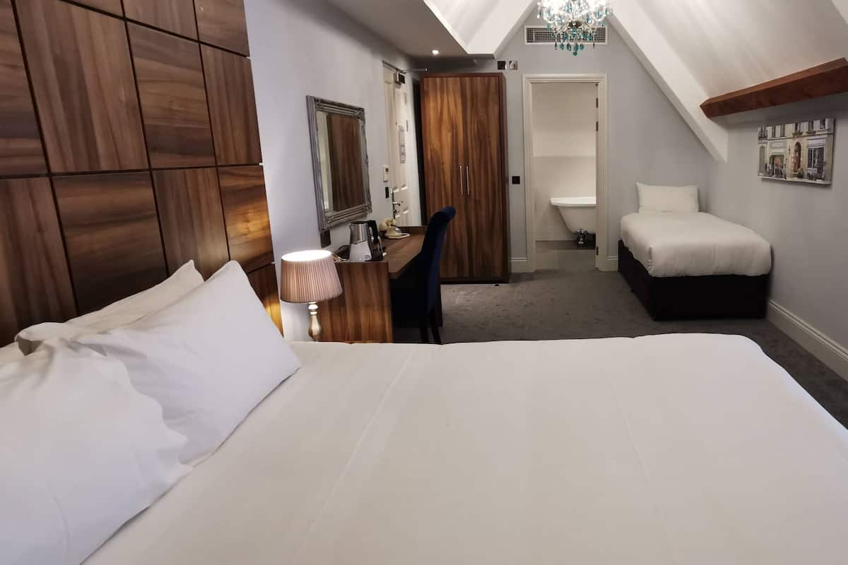 A hotel room with a large bed, a desk with a lamp, a wardrobe, and a small seating area.