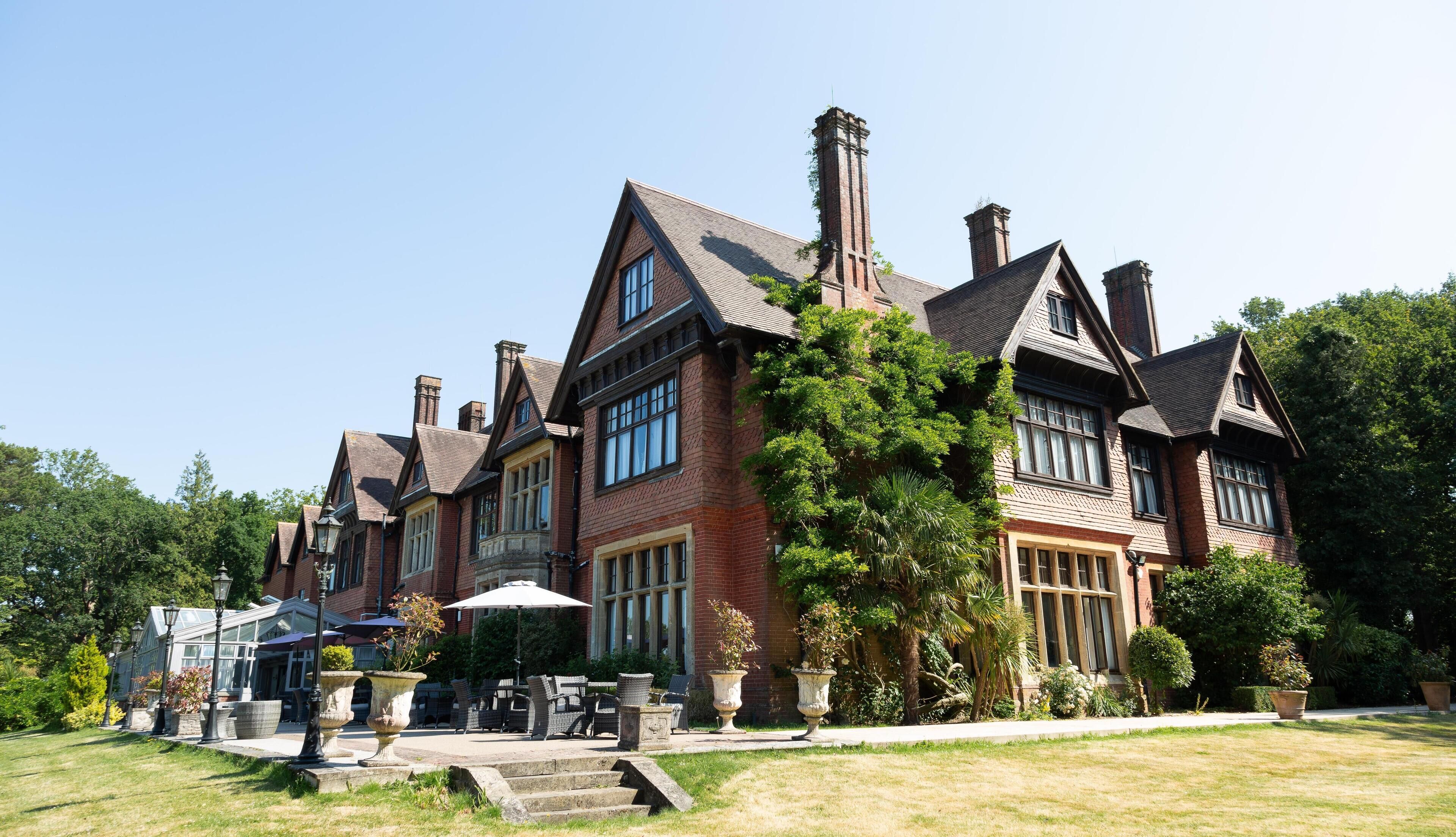 A large, stately building with a symmetrical facade, multiple chimneys, and a well-maintained garden with outdoor seating.