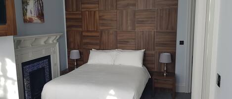 A bedroom with a large bed, wooden headboard, two bedside tables with lamps, and a fireplace.