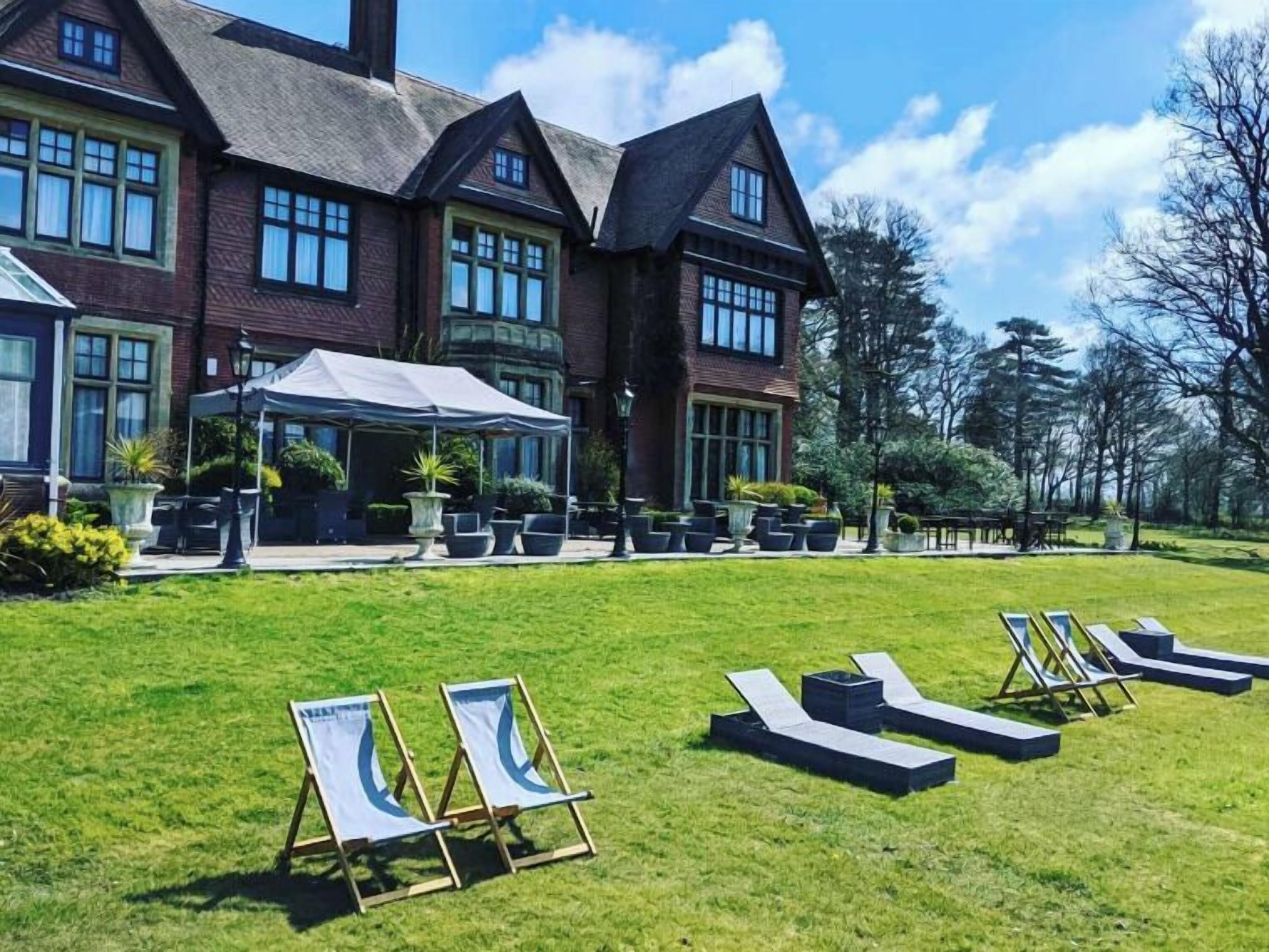 A large brick building with a covered outdoor seating area and lounge chairs on a lawn.