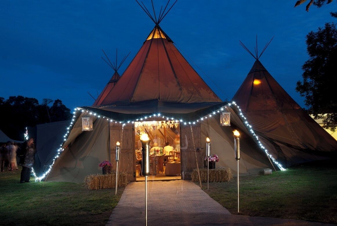 A large teepee with a warm interior, surrounded by string lights and a pathway leading to it.