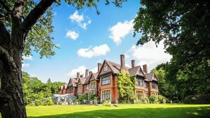 Un grand bâtiment traditionnel en briques, doté de nombreuses cheminées, entouré d’une pelouse bien entretenue et d’arbres.