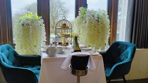Une table dressée pour le thé, avec une théière, des tasses et un présentoir à gâteaux garni de pâtisseries.