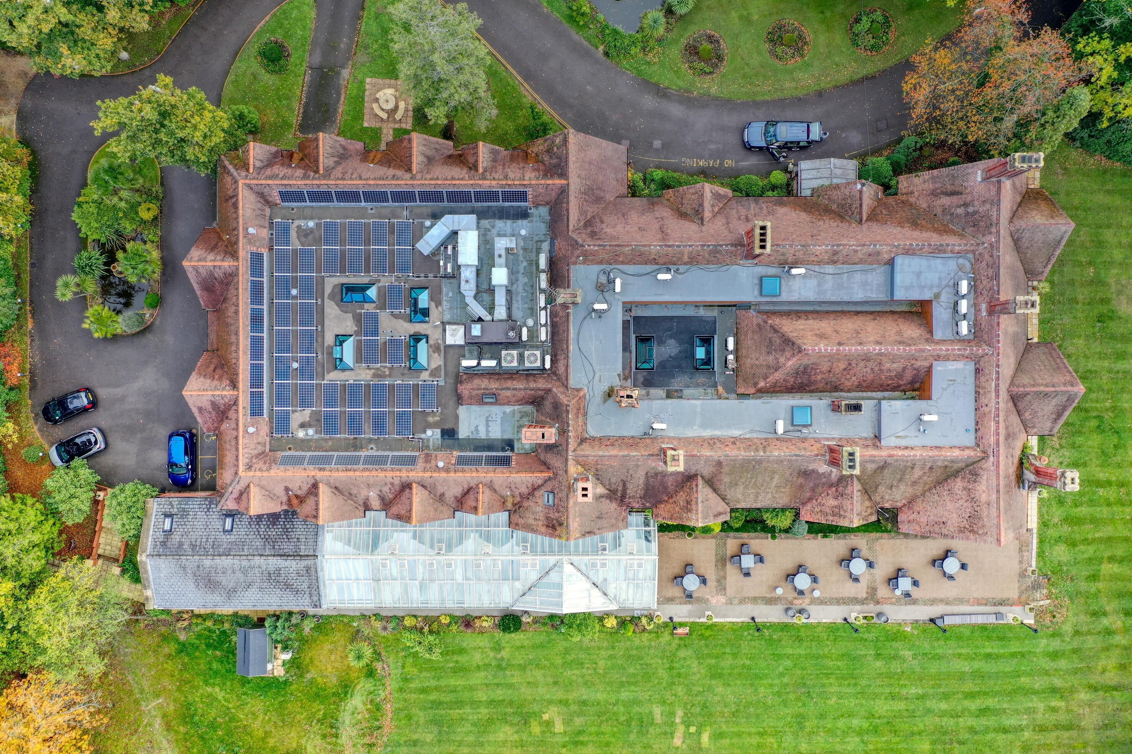 Vue aérienne d’un bâtiment doté d’un parking, de panneaux solaires et d’un espace extérieur aménagé pour s’asseoir.