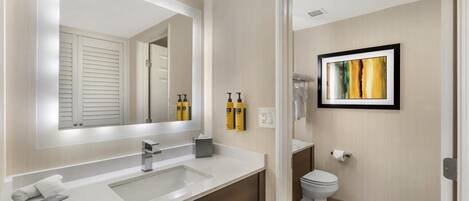 Un bagno moderno con uno specchio grande, un lavandino bianco, un water e un'opera d'arte incorniciata appesa al muro.