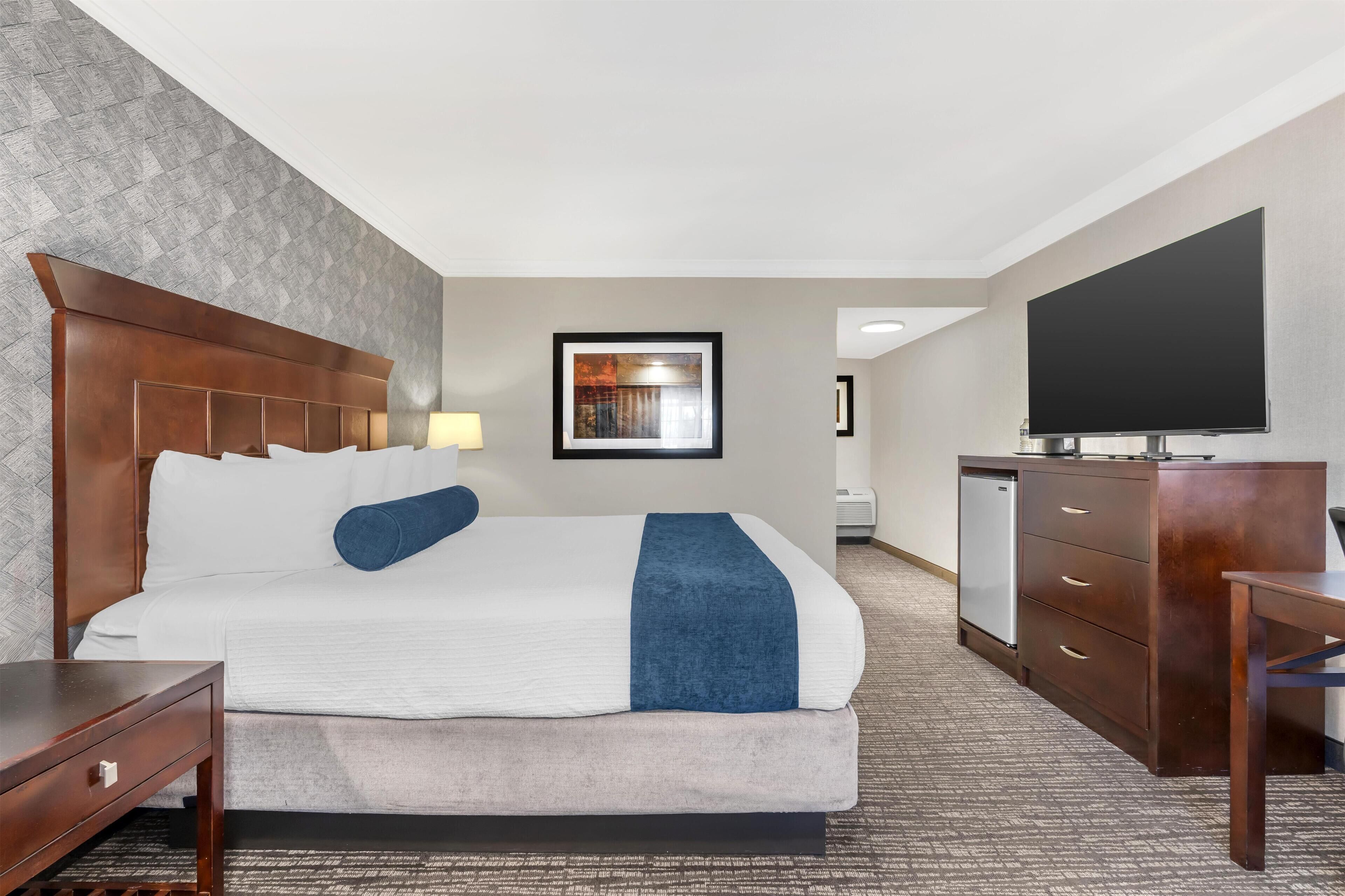 Habitación de hotel con una cama grande, un televisor de pantalla plana, un aparador de madera y un escritorio.