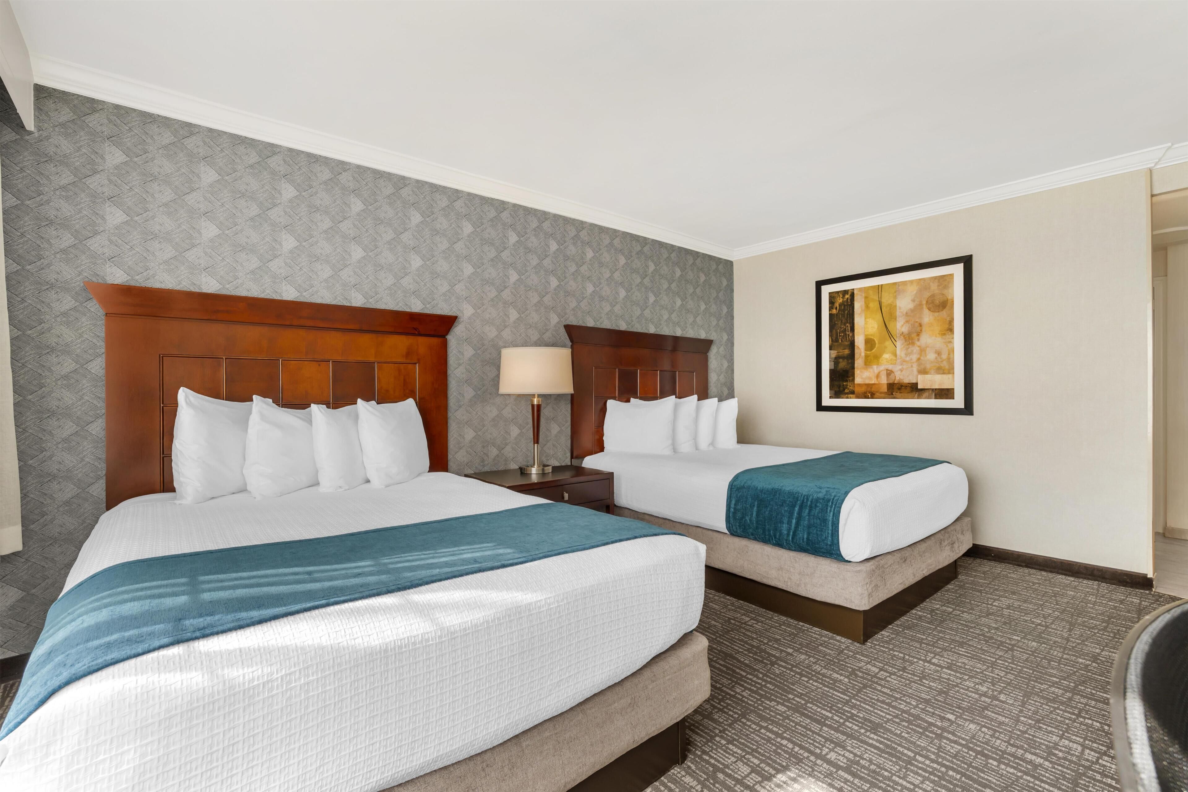 Habitación de hotel con dos camas, un cuadro grande en la pared y una alfombra estampada.