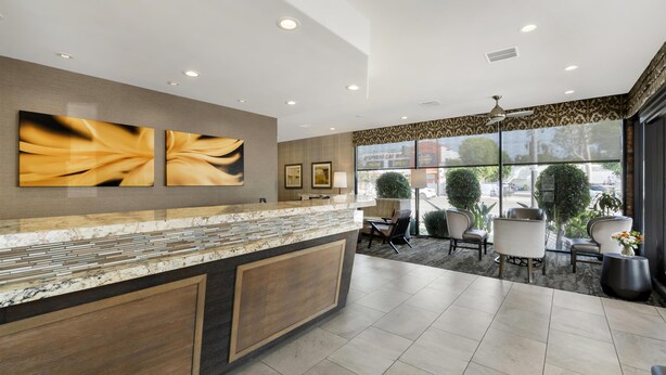 A modern reception area with a marble counter, wooden paneling, and large windows offering a view of the outdoors.
