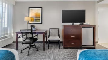 A hotel room with a bed, a desk with a chair, a television, a refrigerator, and a wall-mounted TV.