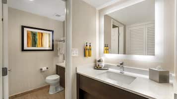 A modern bathroom with a toilet, sink, and mirror. There are toiletries on the sink counter.