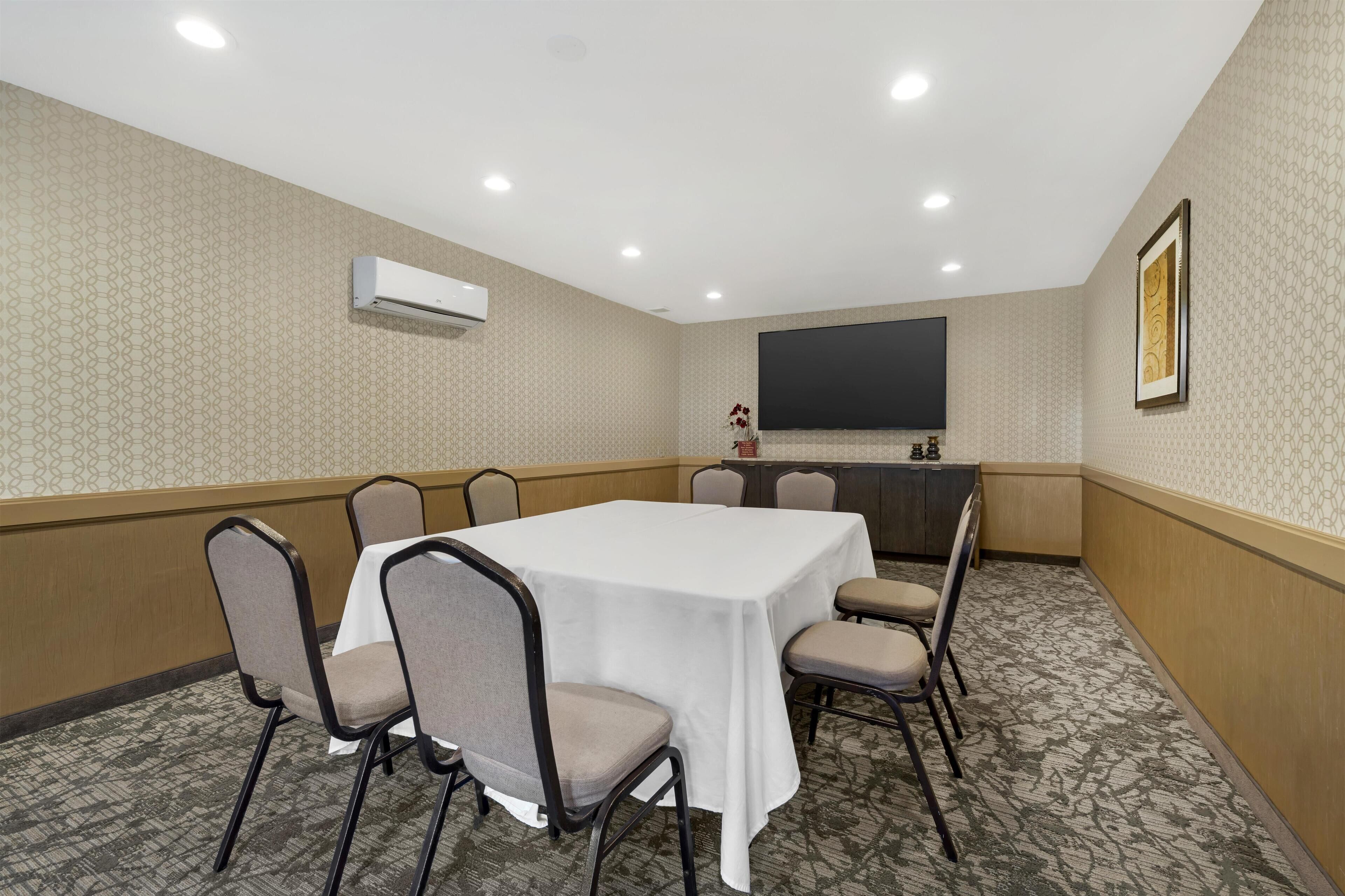 Une salle de conférence avec une table blanche, six chaises, un pupitre et un grand écran.
