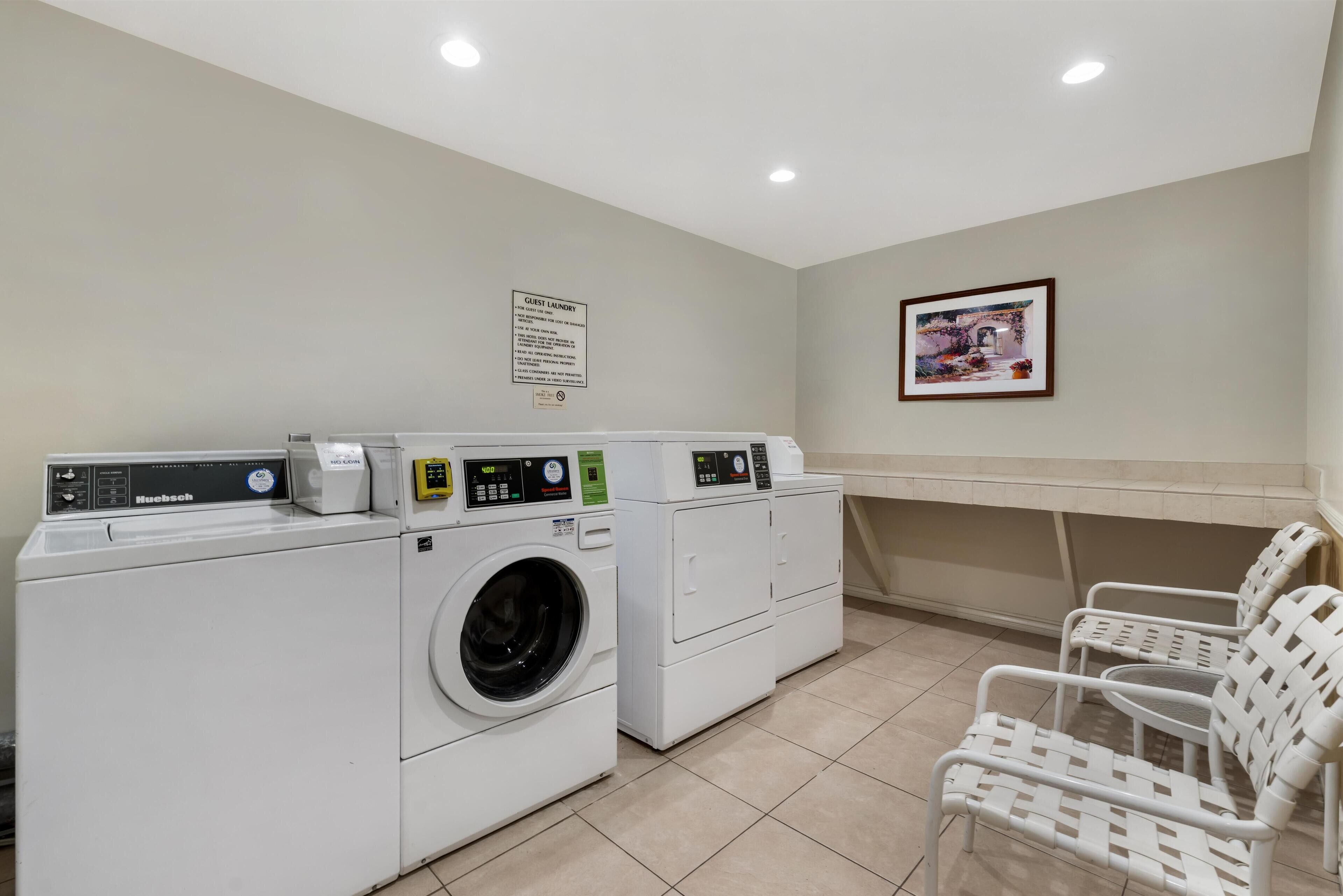 A laundry area with a rack, a washing machine, a dryer, and a chair.