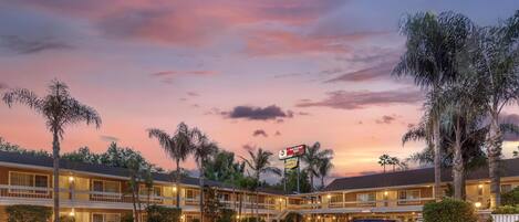 A motel with a two-story structure, a parking lot, and palm trees.