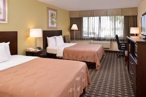 A hotel room with two beds, a desk, a chair, a TV, and a window with curtains. - Quality Inn & Suites Montebello - Los Angeles (Montebello)