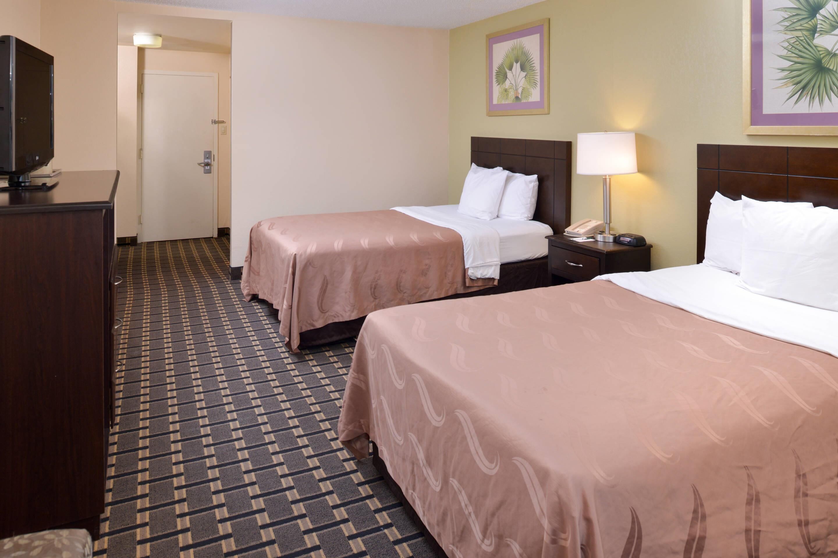 A hotel room with two beds, a TV, a desk, and a lamp.