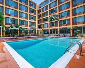 Un hotel con piscina, mobiliario exterior y un edificio de varios pisos con unidades de aire acondicionado.