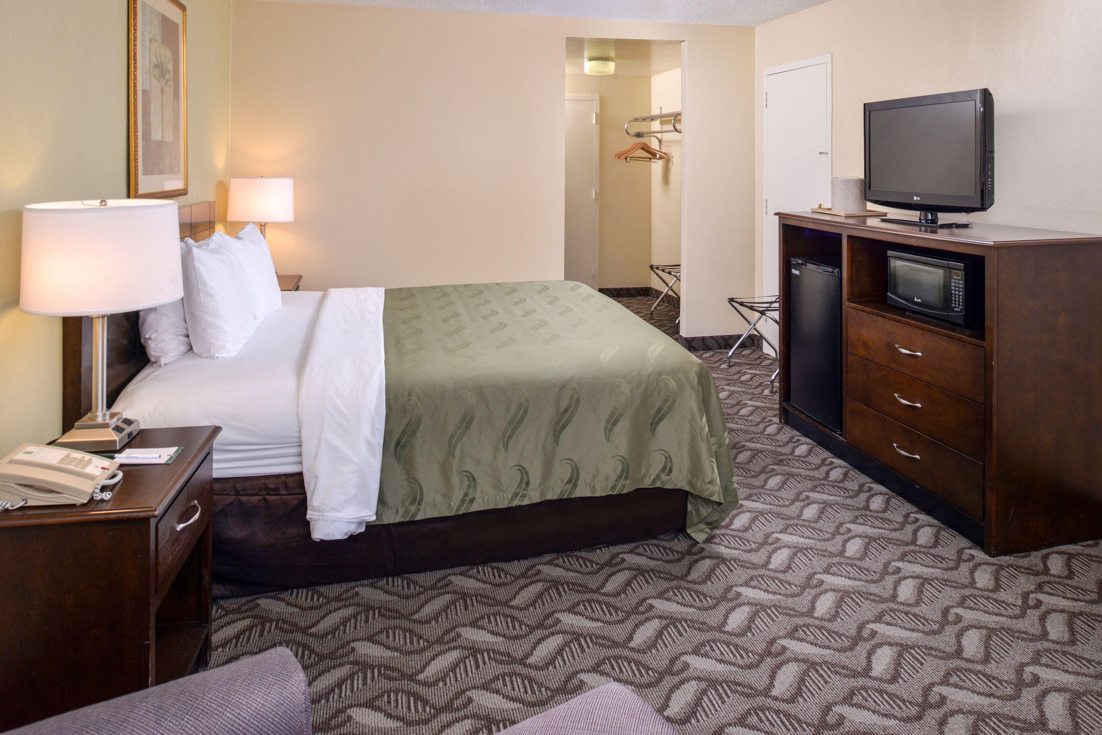 A hotel room with a bed, a desk with a lamp, a television, and a microwave.