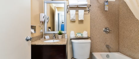 Un baño con lavabo, inodoro y bañera. Hay toallas y artículos de aseo en el mostrador.