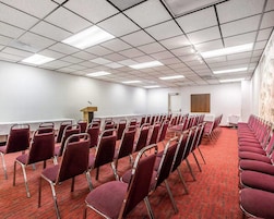 Un salón de conferencias con filas de sillas, un atril y piso alfombrado.