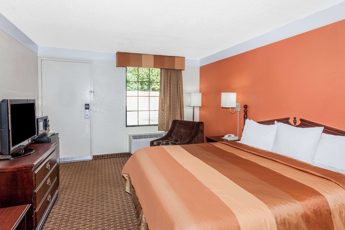 A hotel room with a large bed, a TV on a dresser, a chair, and a window with curtains.