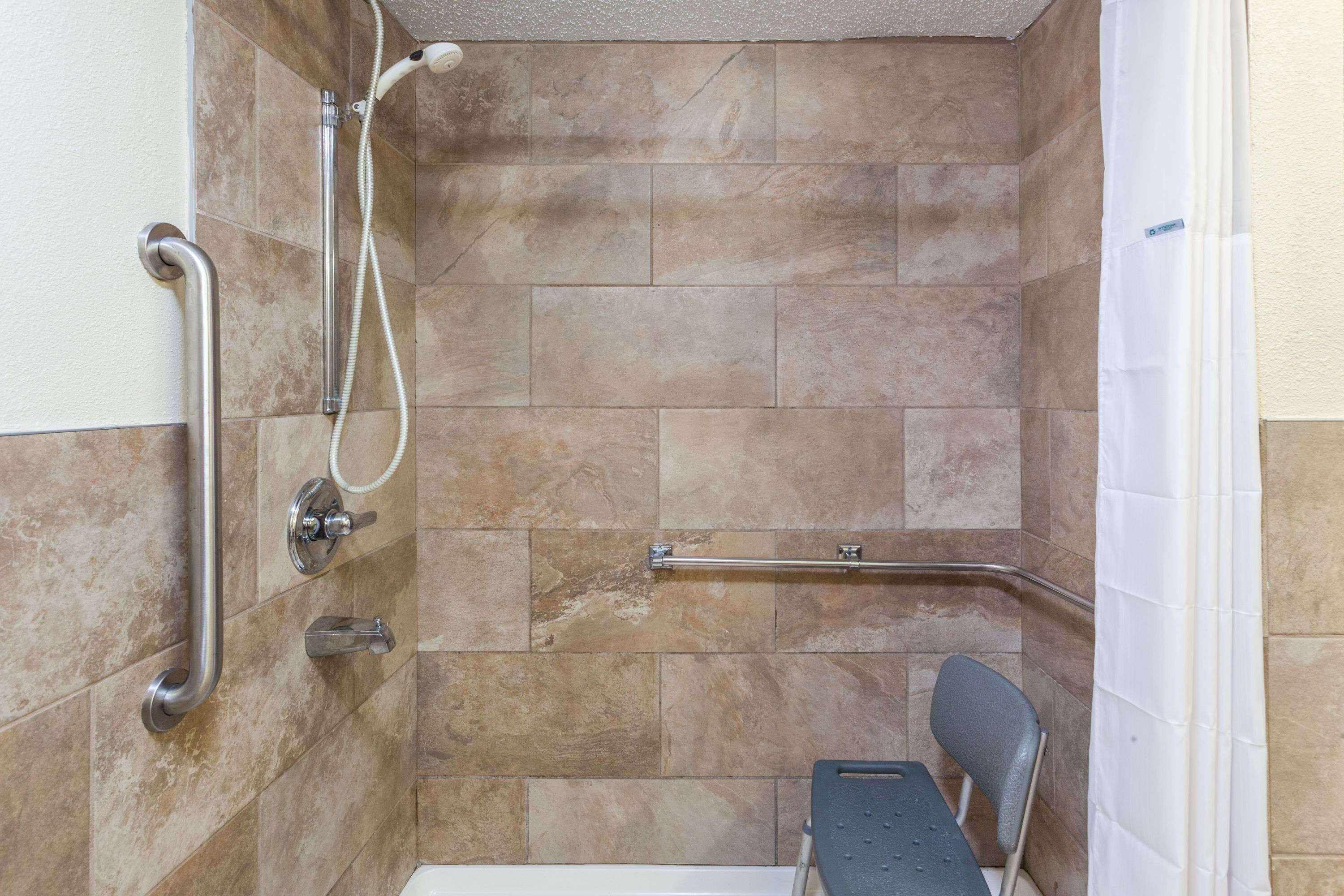 Un espace douche équipé d’une barre d’appui, d’un pommeau de douche à main et d’un siège antidérapant.