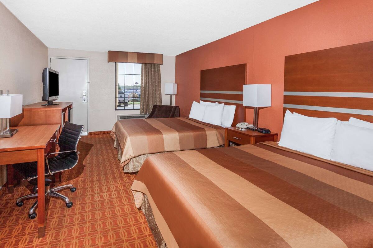 A hotel room with two beds, a desk, a chair, a TV, and a window with curtains.
