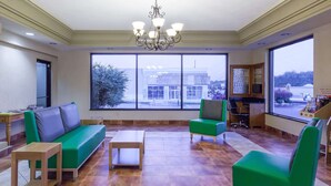 A spacious room with a green sofa, a small table, and a chair. There is a large window with a view of buildings outside. - Days Inn by Wyndham Dalton (Dalton)