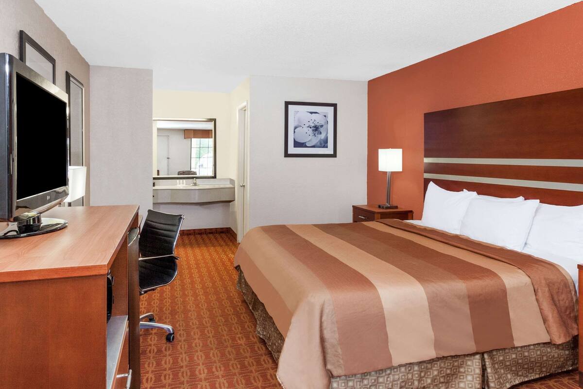 A hotel room with a bed, desk, chair, television, and a bathroom visible through an open door.