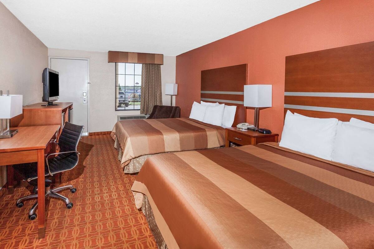 A hotel room with two beds, a desk, a chair, a television, and a window with curtains.