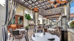 An outdoor patio with round tables and wicker chairs, a ceiling fan, and a grill.