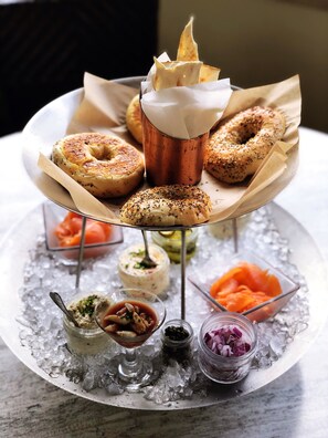 A three-tiered tray with bagels and various spreads on ice.