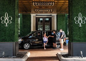 A black vehicle with "Bellasera Resort" branding parked at a resort entrance with a green hedge and a decorative light fixture above.