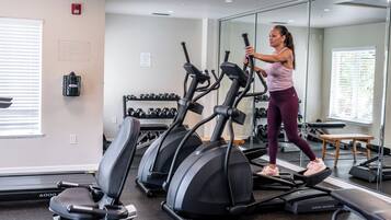 Un gimnasio con cintas de correr, mancuernas y un espejo.