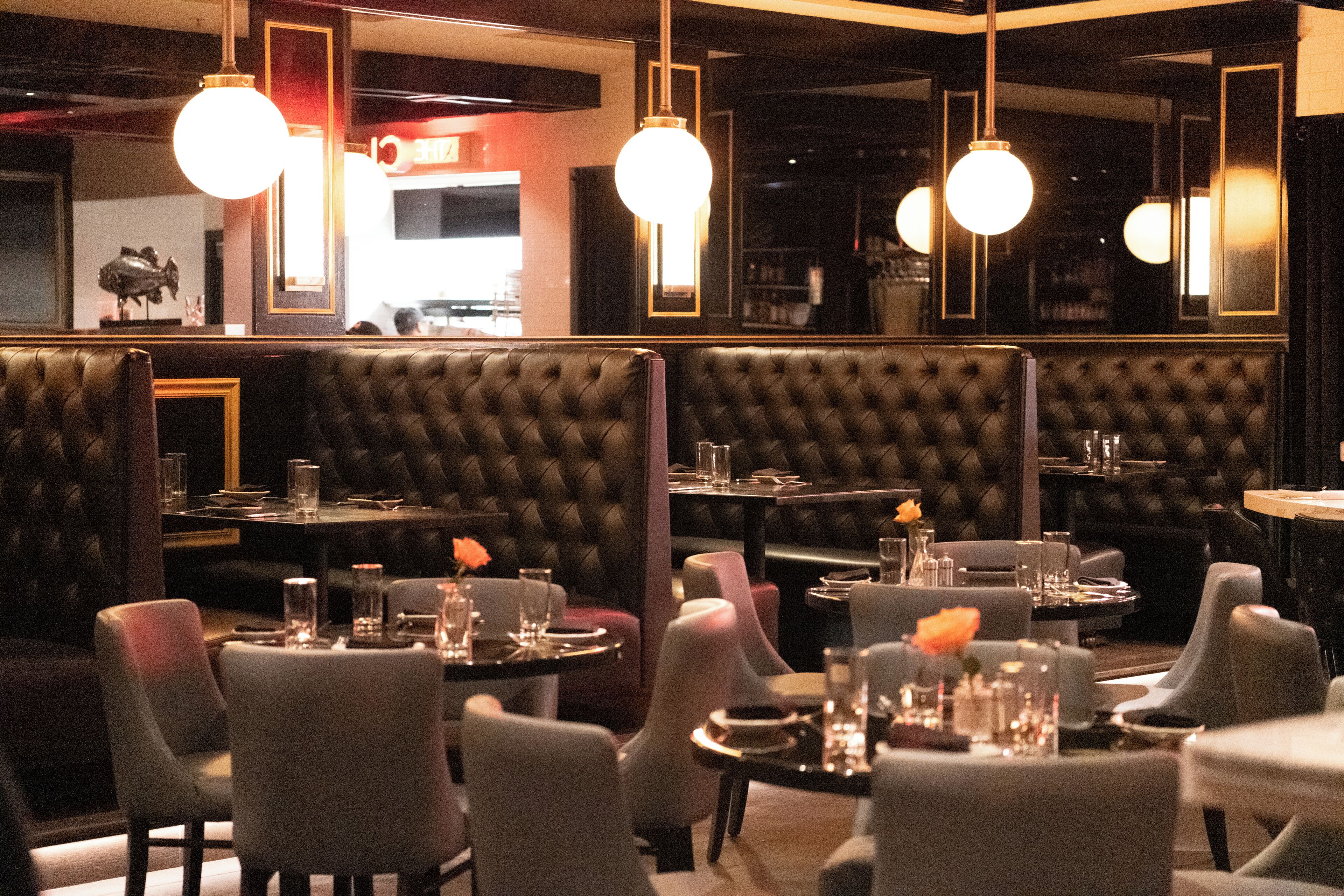 Un restaurante con asientos tipo cabina y mesas redondas, con un interior oscuro e iluminación colgante.