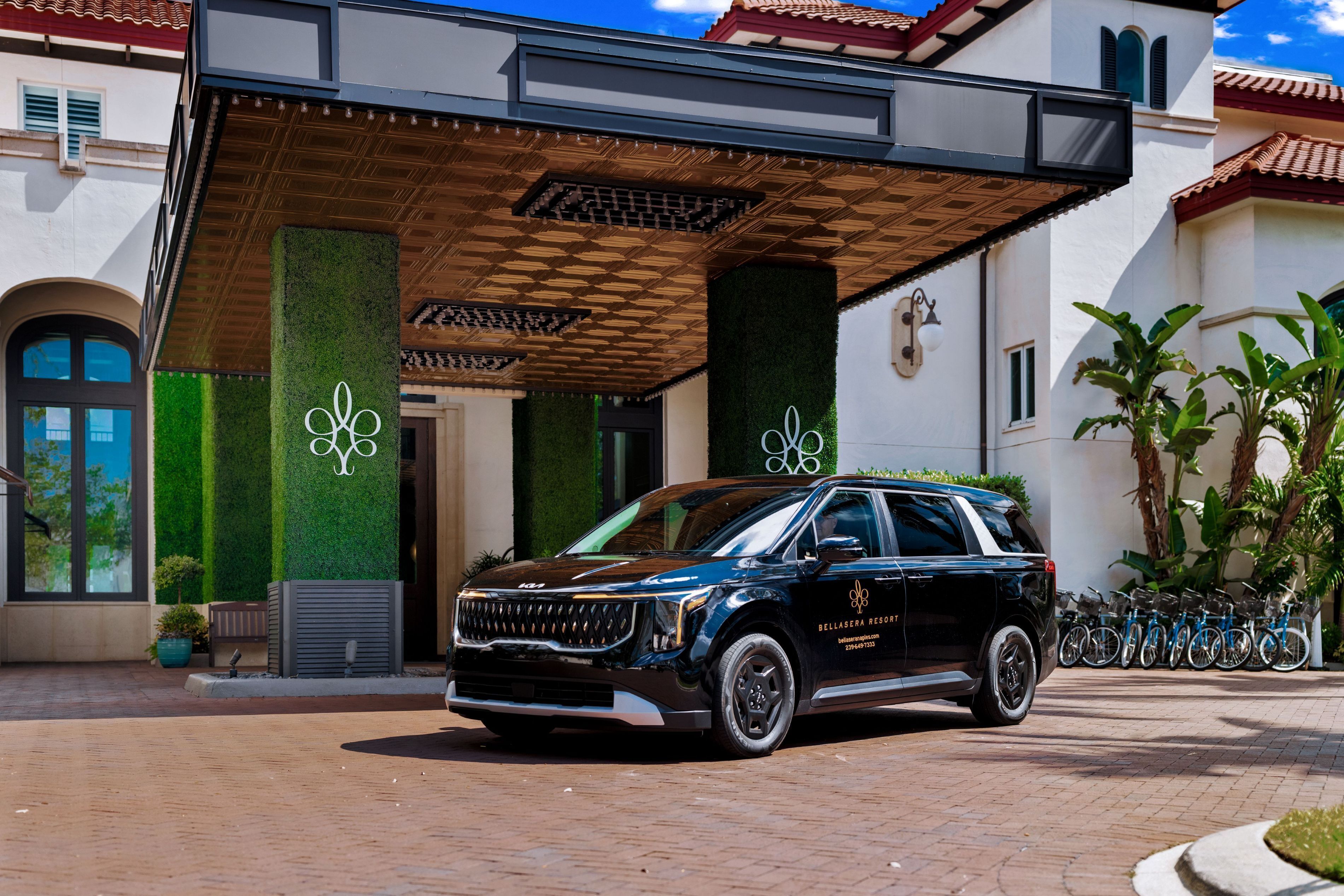 A black SUV parked in front of a building with a covered entrance, a logo on the wall, and a bike rack to the right.