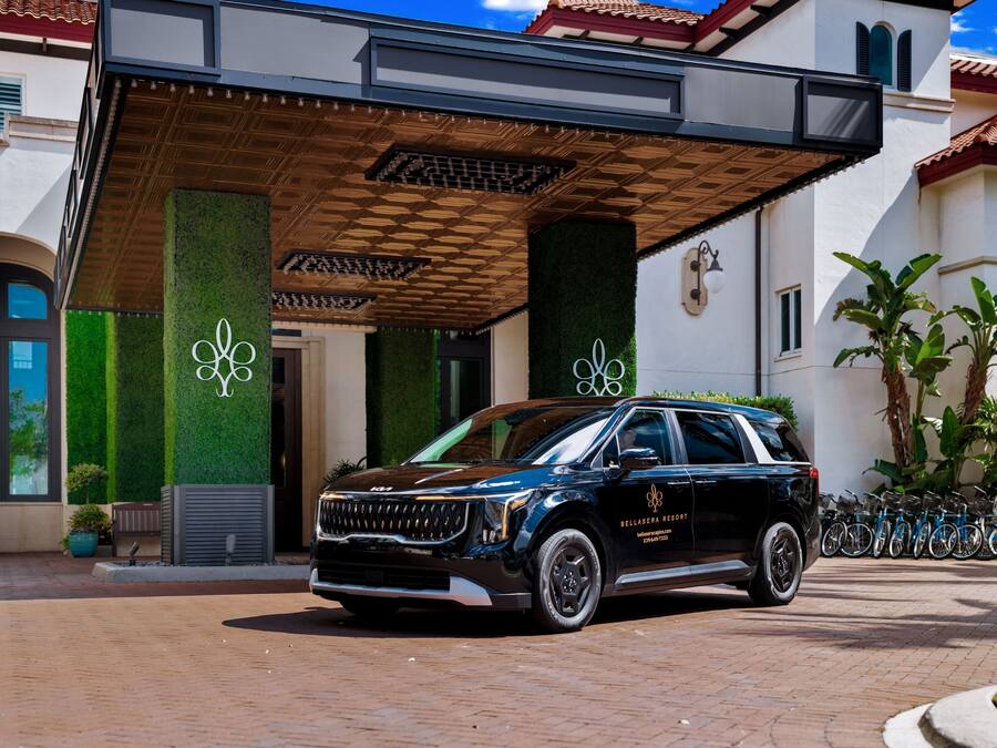 A black SUV parked in front of a building with a covered entrance, a logo on the wall, and a bike rack to the right.
