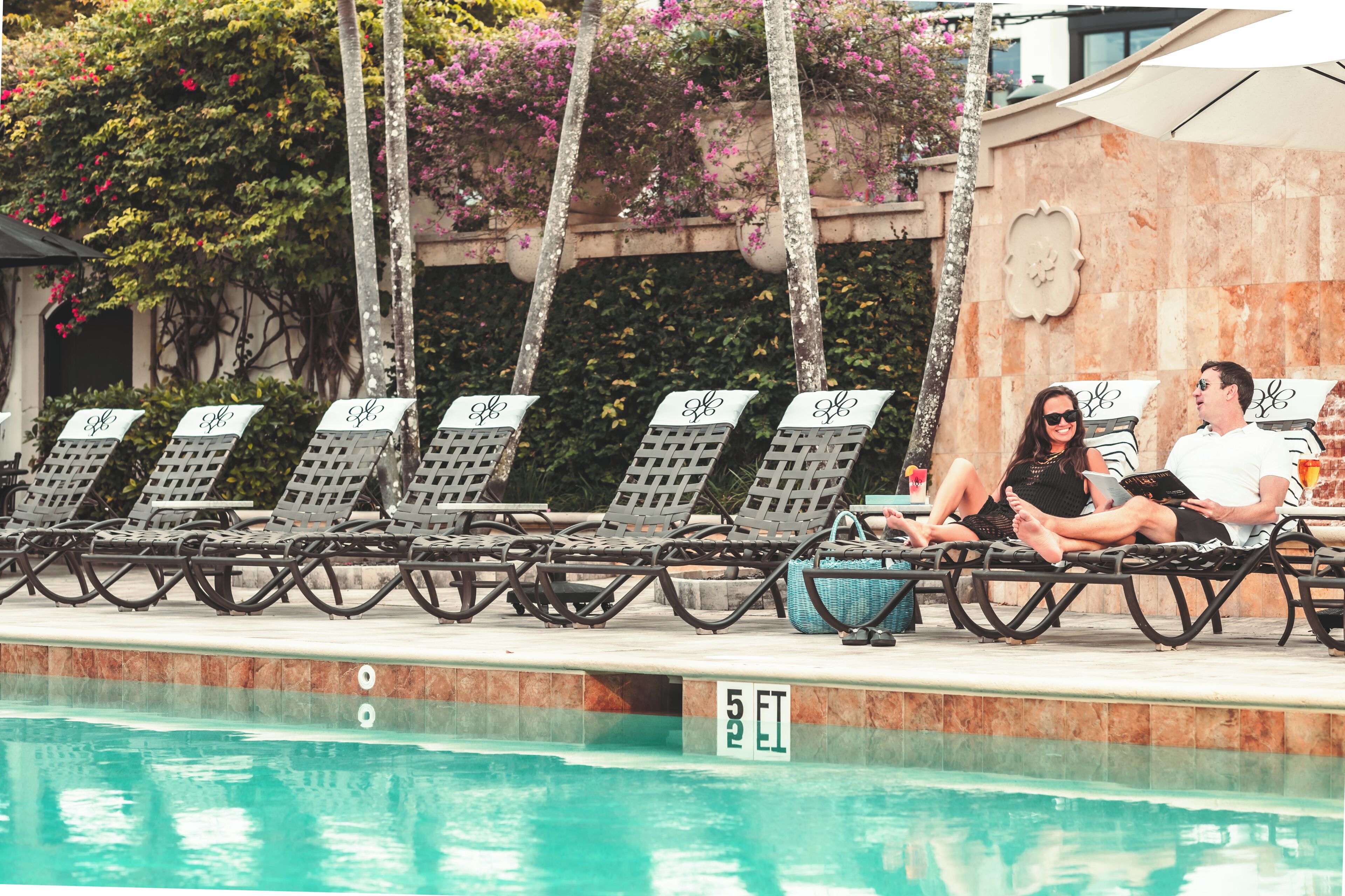 A poolside area with lounge chairs, a pool, and a stone wall with climbing plants.