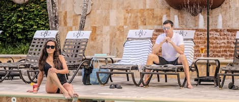 A poolside area with lounge chairs, a fountain, and a stone wall.