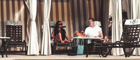 A poolside area with two lounge chairs, a table with a drink, and a sign indicating the pool's depth.