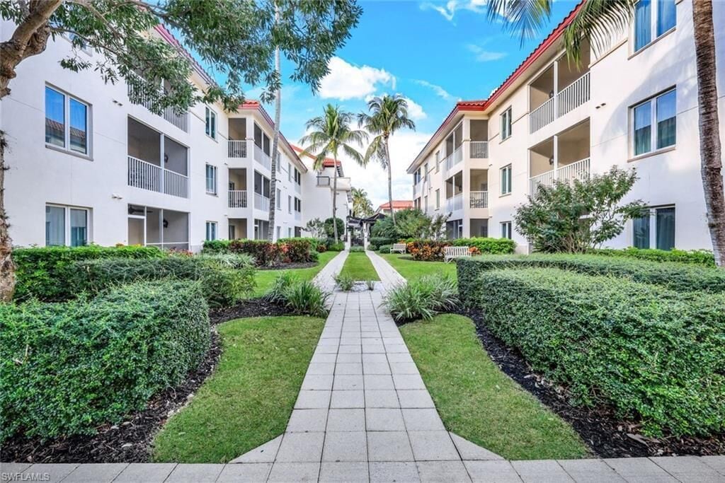 A pathway leading to a building with multiple balconies, surrounded by well-maintained greenery and palm trees.