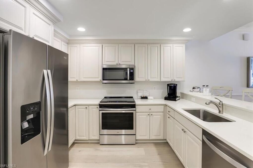 A modern kitchen with white cabinetry, stainless steel appliances, and a built-in oven.