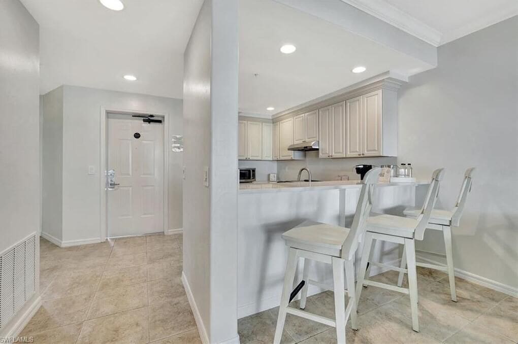 Una cocina moderna con armarios blancos, una isla central con taburetes y luces empotradas en el techo.