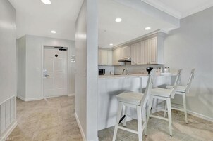 Una cocina moderna con armarios blancos, una isla central con taburetes y luces empotradas en el techo.