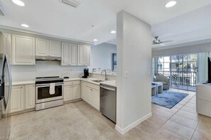 A modern kitchen with white cabinets, stainless steel appliances, and a large window overlooking a balcony.