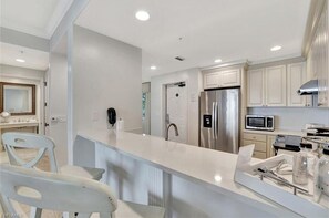 A modern kitchen with white cabinetry, stainless steel appliances, and a white countertop.