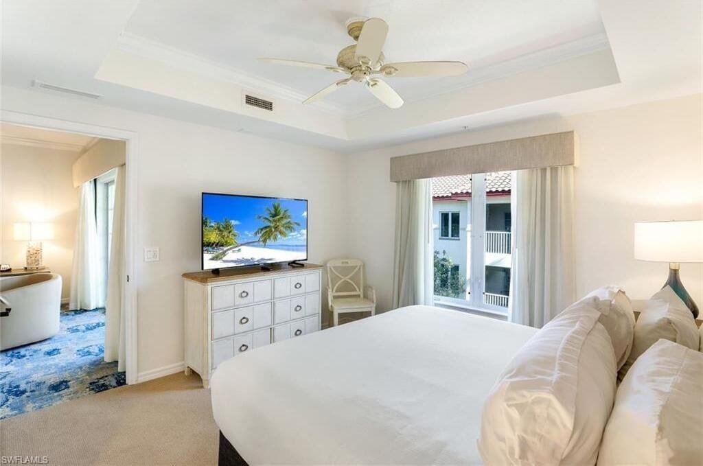 A hotel room with a large bed, a ceiling fan, a television on a dresser, a chair, and a balcony with curtains.