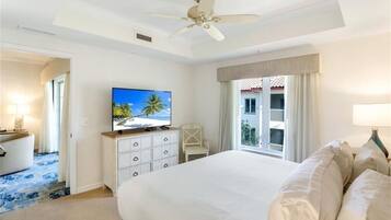 Camera d'albergo con un letto grande, una ventola a soffitto, una televisione su un comò, una sedia e un balcone con tende.