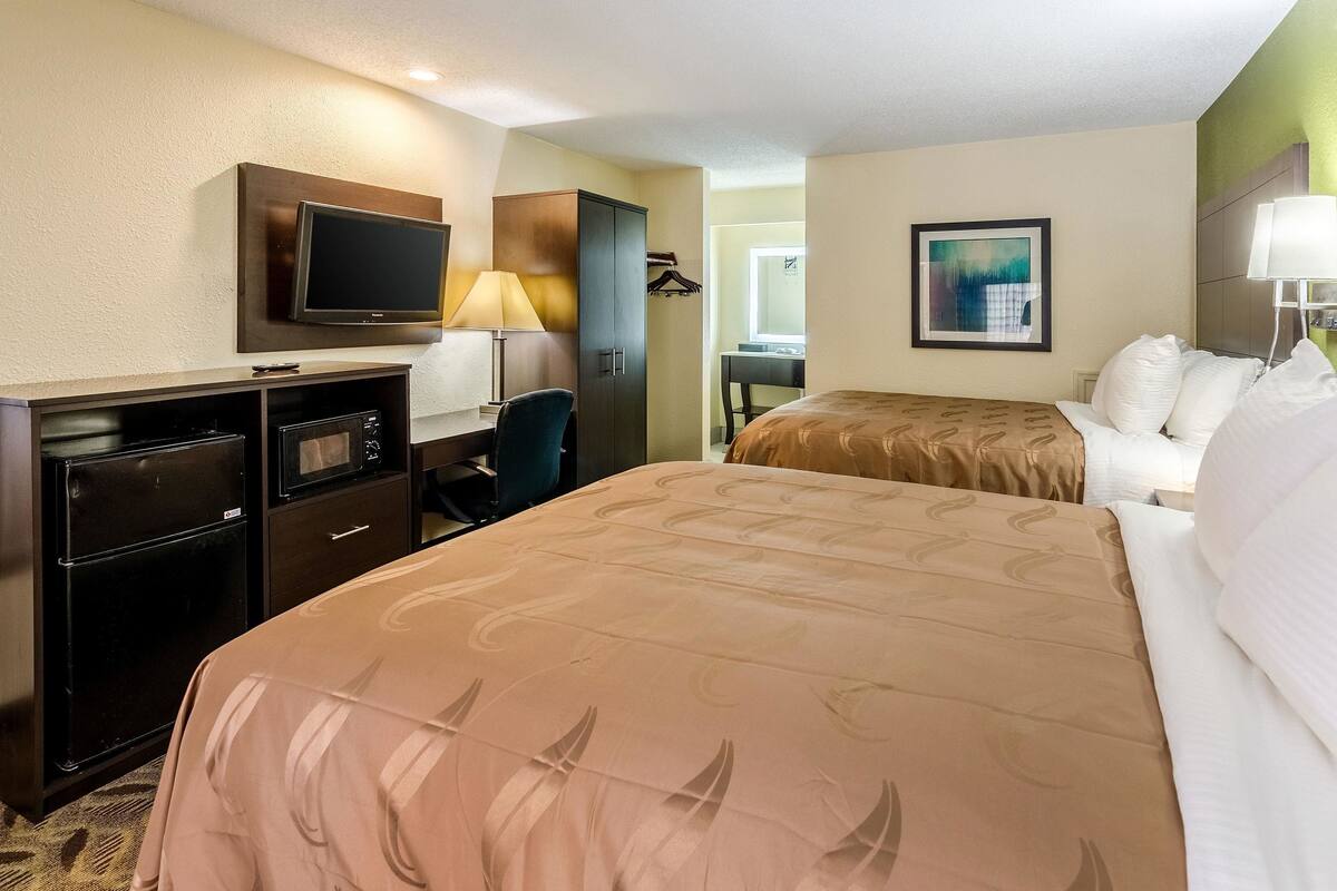 A hotel room with a bed, a desk with a computer, a TV, and a wardrobe.