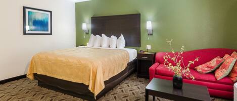 Une chambre d’hôtel avec un lit, un canapé rouge, une petite table avec un vase et un tableau encadré au mur.